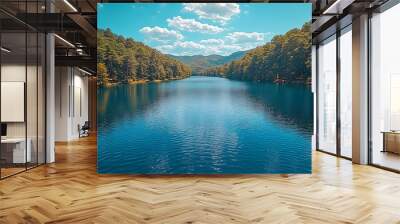 Tranquil lake surrounded by lush green forest under a blue sky with white clouds. Wall mural