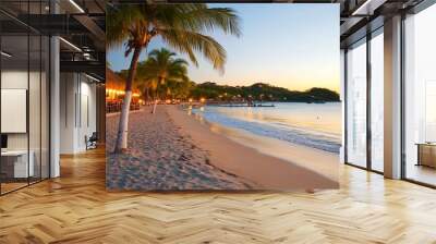 Tropical beach at sunset with palm trees and a restaurant. Wall mural