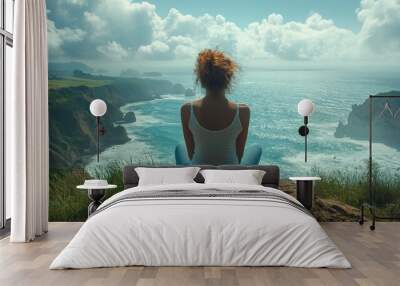 Woman sits on a cliff overlooking the ocean with cloudy skies. Wall mural