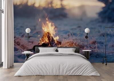 A campfire crackles in the middle of a snowy field, casting a warm glow against the white backdrop Wall mural