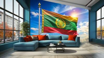 A vibrant waving national flag with golden threads and intricate embroidery proudly hoisted on a flagpole against a clear blue sky with fluffy white clouds. Wall mural