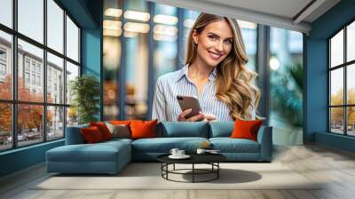 Attractive young adult woman with shoulder-length hair and casual attire holds a smartphone, focused on the screen with a subtle smile indoors. Wall mural