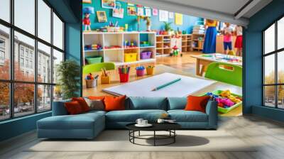 Colorful kindergarten classroom background with various children's artwork and toys, a clipboard with papers and a pen lie on a table, indicating a teacher's presence. Wall mural