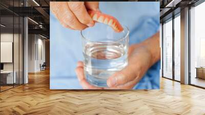 Asian senior woman patient clean teeth denture in a glass with solution for chew food. Wall mural