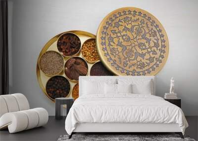 Spice box or collection of Indian spices or Garam Masala like cumin seeds, coriander, Fenugreek, big cardamom, black pepper, cloves, mustard seeds in designer brass container on wooden background Wall mural