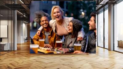 group of friends smiling and drinking at brewery, meeting of couple of millennials toasting with beers and eating fusion food, nightlife and social gathering of young people after covid19 outbreak Wall mural