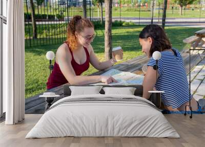 two young woman planning the sightseeing of a city, female tourists looking at map for travel destination, resumption of holiday activities after the lockdown for Coronavirus Wall mural