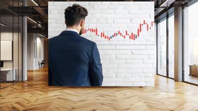 A businessman observes a upward-trending stock market graph on a modern wall, contemplating investment strategies. Wall mural