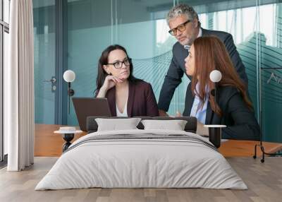 Businesspeople watching and discussing presentation on pc while sitting and standing at meeting table together. Medium shot. Communication and teamwork concept Wall mural