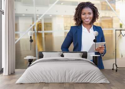 Businesswoman holding tablet pc and smiling at camera. Cheerful young African American businesswoman holding digital tablet and looking at camera. Wireless technology concept Wall mural