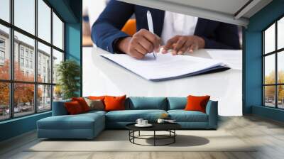 Businesswoman signing contract. African American business woman sitting at table in office, holding pen and writing in document. Legal expertise concept Wall mural