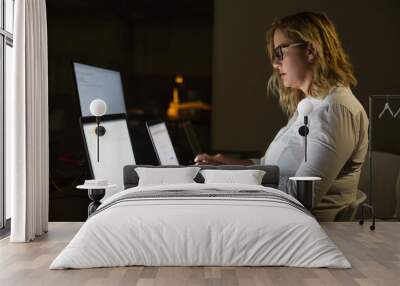 Businesswoman using laptop in dark office. Side view of focused middle aged businesswoman sitting in dark office and working with computer late at night. Overworking concept Wall mural