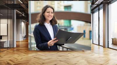 Cheerful businesswoman holding folder. Smiling middle aged businesswoman in formal wear holding papers and looking aside on street. Professional occupation concept Wall mural