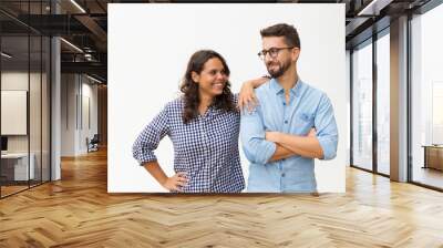 Cheerful couple standing close together, chatting and laughing. Young woman in casual and man in glasses posing isolated over white background. Friendship in couple concept Wall mural