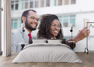 Cheerful diverse business team taking selfie outside. Happy business man and woman holding smartphone, posing and smiling at screen. United team and selfie concept Wall mural