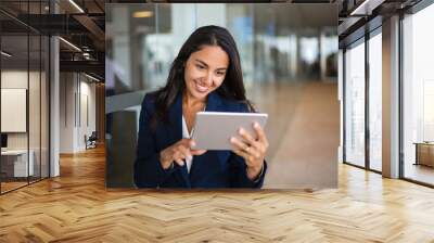 Cheerful happy office worker using tablet in office hall. Young Latin business woman leaning on glass wall and reading on screen. Tablet computer concept Wall mural