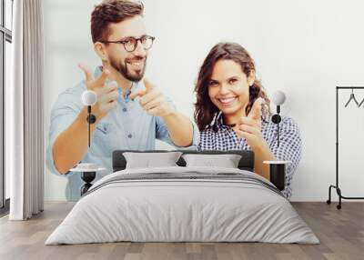 Cheerful positive couple pointing fingers at camera. Young woman in casual and man in glasses posing isolated over white background. Choosing you concept Wall mural