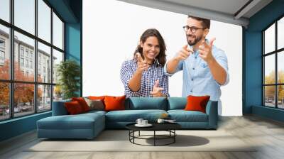 Cheerful positive couple pointing fingers at camera. Young woman in casual and man in glasses posing isolated over white background. Choosing you concept Wall mural