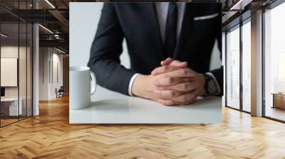 Closeup of thoughtful entrepreneur with clasped hands. Business man wearing suit and sitting at table with tea cup. Contemplation or waiting concept. Cropped front view. Wall mural