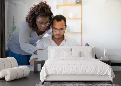 Concentrated African American woman pointing at laptop. Focused colleagues working with laptop at office. Teamwork concept Wall mural