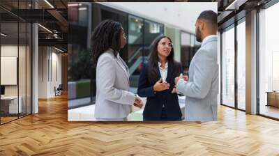 Confident female agent telling customers about project in office hall. Business man and women standing in hallway, talking and gesturing. Business meeting concept Wall mural