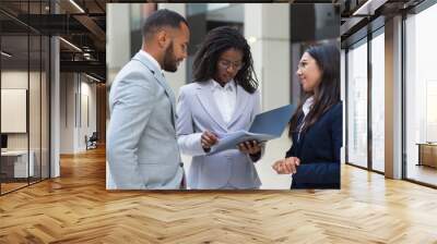 Confident friendly diverse business people discussing agreement in office hall. Business man and women standing in hallway, talking and reading document. Agreement concept Wall mural