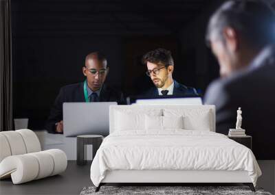 Confident people discussing new project in office late at night. Thoughtful business team sitting at long table with laptops. Teamwork, working late concept Wall mural