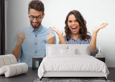 Content young couple celebrating success. Front view of cheerful young man and woman gesturing with hands and triumphing on white background. Winner concept Wall mural