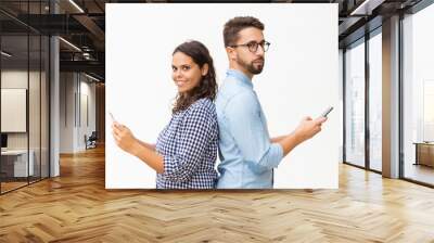 Couple standing back-to-back and using cellphones. Young woman in casual and man in glasses posing isolated over white background. Communication concept Wall mural