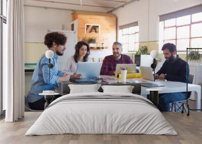 Creative group working on startup, using laptops in modern co-working with potted plant. Business colleagues in casual sitting together in contemporary office space. Teamwork concept Wall mural