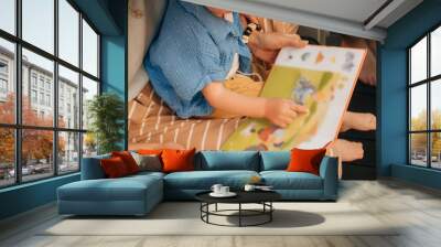 Cute little girl pointing at pictures in book. Toddler sitting on her mother laps and reading book. Family at home, child development concept Wall mural