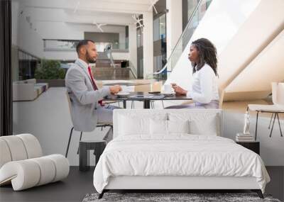 Diverse business colleagues having coffee break in office hall. Business man and woman sitting at table in cafe, drinking coffee and talking. Business morning concept Wall mural