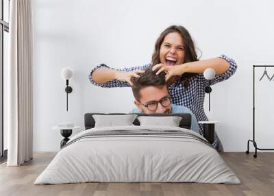 Excited joyful woman setting funny hair of her happy boyfriend. Young woman in casual and man in glasses standing isolated over white background. Fun and joy together concept Wall mural