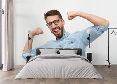 Excited young man showing biceps. Handsome happy young man in eyeglasses showing muscles and smiling at camera on white background. Muscles concept Wall mural