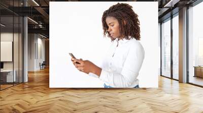 Focused employee texting message on smartphone. Young African American office worker standing isolated over white background. Mobile phone using concept Wall mural