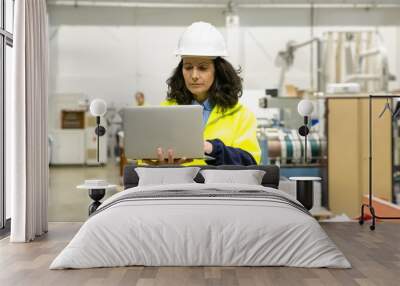 Focused female technician using laptop at printing house. Concentrated factory employee standing with open laptop at workplace. Print manufacturing concept Wall mural