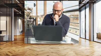 Focused middle-aged man working on laptop in street cafe Wall mural