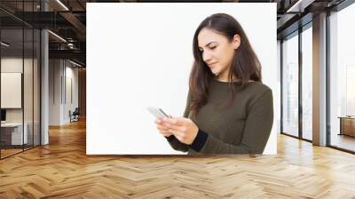 Focused serious cellphone user texting message. Young woman in casual with mobile phone standing isolated over white background. Wireless technology concept Wall mural