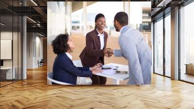 Happy business partners meeting in outdoor cafe and greeting each other. Business man and women standing and sitting at table outdoors, shaking hands, talking and smiling. Partners meeting concept Wall mural