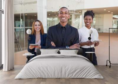 Happy cheerful business people posing in office hallway. Three multiethnic workers in formal suits standing for camera indoors and smiling. International cooperation concept Wall mural