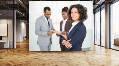 Happy confident female business leader posing while her team working. Middle aged businesswoman standing with arms folded and smiling. Successful business woman concept Wall mural