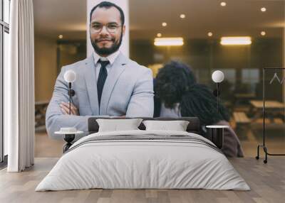 Happy confident male professional posing with arms folded, looking at camera, smiling. Her multiethnic colleagues working in background. Successful team leader concept Wall mural