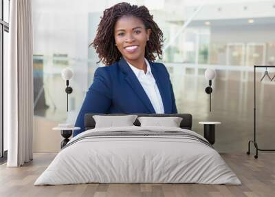 Happy confident professional posing near office building. Young African American business woman standing outside, adjusting formal jacket, looking at camera, smiling. Successful businesswoman concept Wall mural