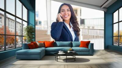 Happy confident professional talking on cellphone outside. Beautiful young Latin woman in office suit calling on phone during work break. Business phone talk concept Wall mural