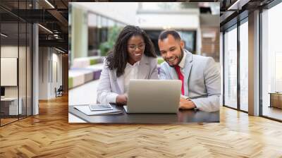 Happy excited colleagues using laptop for video call. Business man and woman sitting in office lobby, staring at computer monitor, smiling and speaking. Video chat concept Wall mural