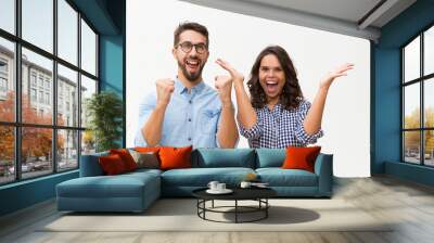 Happy excited couple rejoicing at good news, making winner gestures, celebrating success. Young woman in casual and man in glasses standing isolated over white background. Good news concept Wall mural