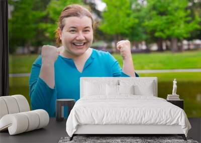 Happy excited plus sized woman celebrating success. Cheerful Caucasian lady making winner gesture with both hands and smiling at camera. Winning concept Wall mural