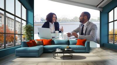 Happy female mentor explaining work issues to male intern. Business man and woman sitting at meeting table with open laptop and talking. Partnership concept Wall mural