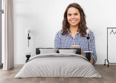 Happy joyful female customer holding cell and looking at camera. Young woman in casual checkered shirt standing isolated over white background. Happy cellphone user concept Wall mural