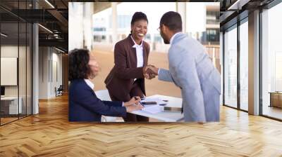 Happy sales agent welcoming customer in outdoor cafe. Business man and women standing and sitting at table outdoors, shaking hands and smiling. Business meeting outside concept Wall mural